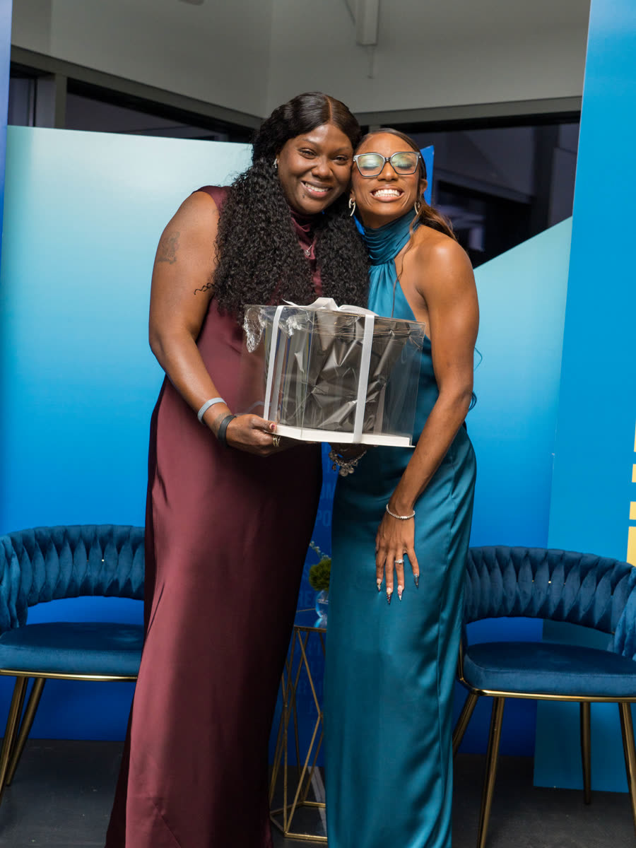 Sonia Collier receiving an award from Melissa Jefferson-Wooden on stage for her contribution to The Village Initiative